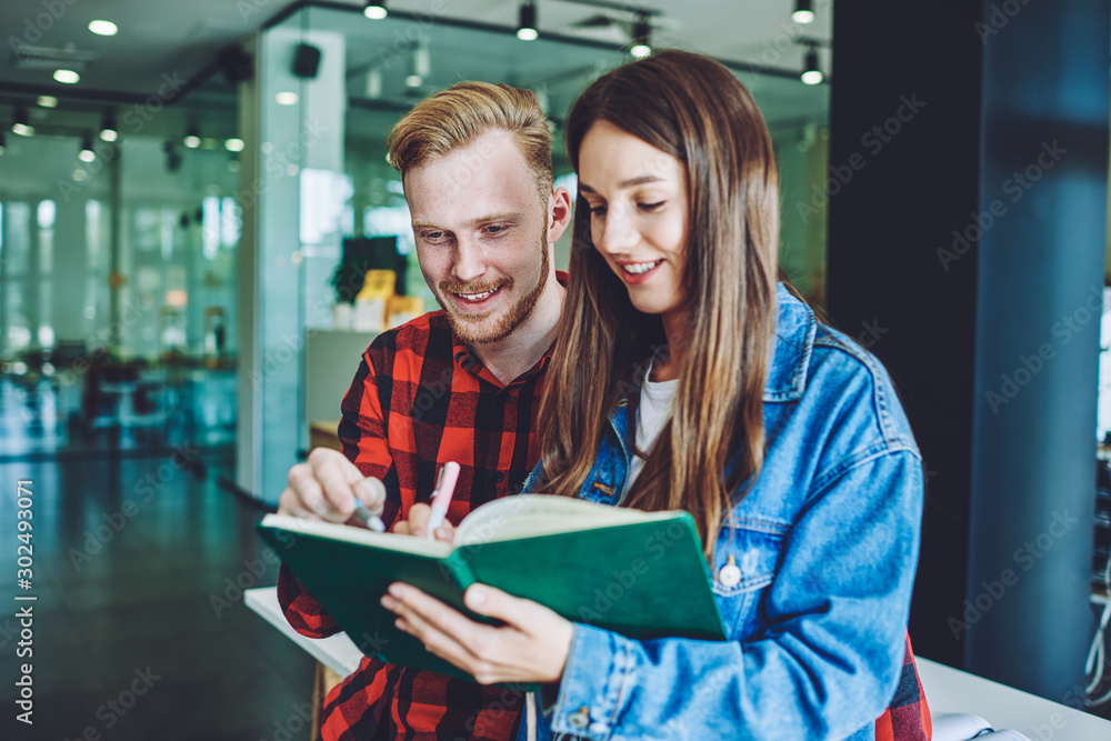 Positive male and female students collaborating in university campus doing school homework togetherness, happy successful friends preparing to upcoming examination writing information in textbook Positive male and female students collaborating in university campus doing school homework togetherness, happy successful friends preparing to upcoming examination writing information in textbook