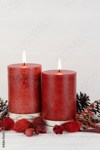 Burning red Christmas candles on a rustic white wooden background with natural potpourri elements and pine cones. Vertical photo