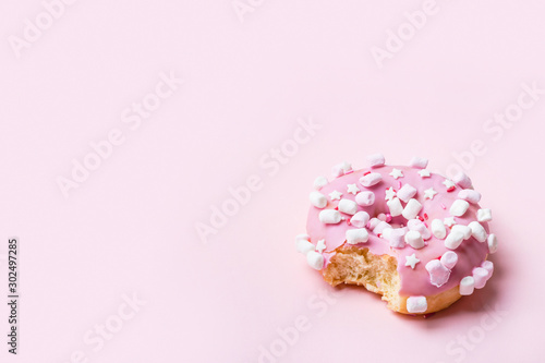 Bitten Pink donut with marshmallows and sprinkled. Minimal concept