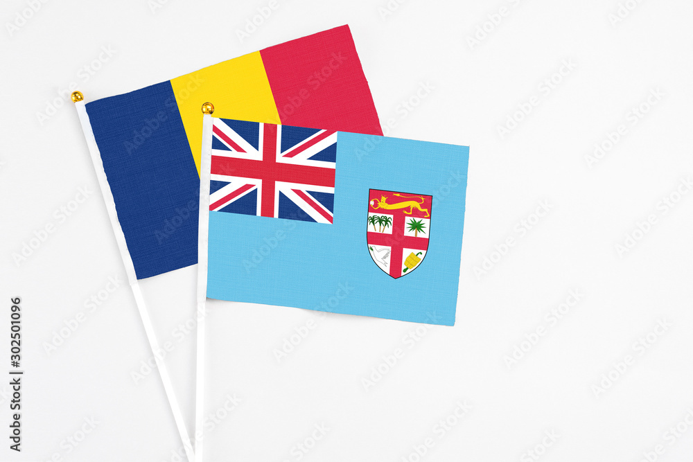 Fototapeta premium Fiji and Chad stick flags on white background. High quality fabric, miniature national flag. Peaceful global concept.White floor for copy space.