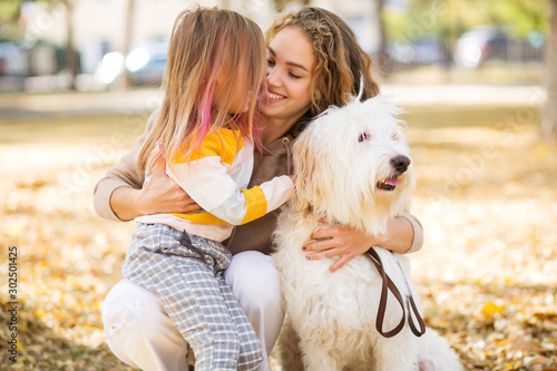 Beautiful, happy young mother with little girl and dog outdoor.
