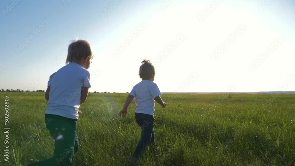 Two children in white t-shirts running on green fresh grass. Happy children enjoy life. The concept of teamwork. Two children in white t-shirts running on green fresh grass. Happy children enjoy life. The concept of teamwork.