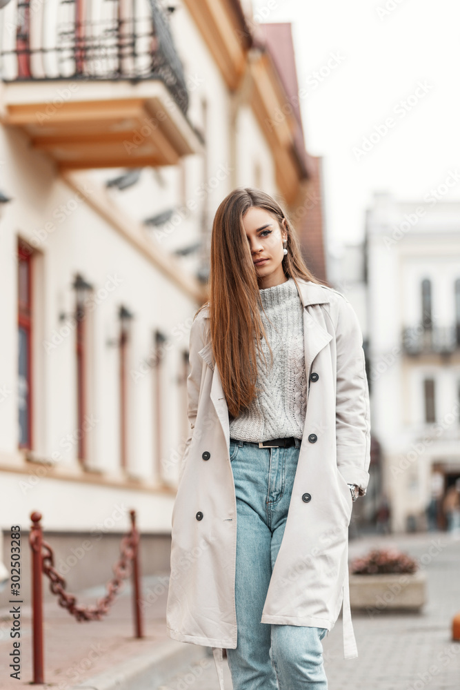 Modern young fashionable woman in stylish autumn-spring clothes walks on a  street near vintage buildings. Urban girl fashion model in elegant  outerwear travels on the city. Trendy women's clothing. Stock Photo