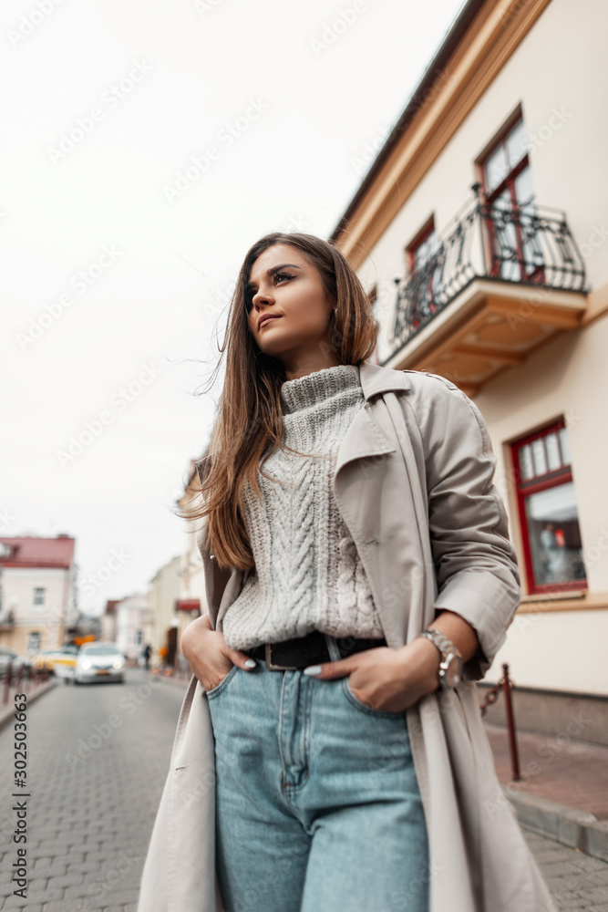European young modern woman in stylish autumn spring clothes stands on a street in the city near vintage buildings. Trendy girl model in fashionable outerwear outdoors. Seasonal women s clothing. Stoc...