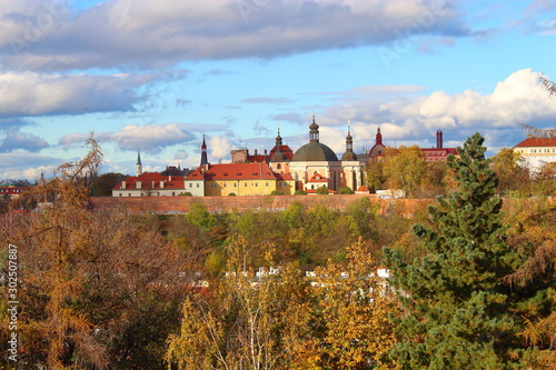 View of the old buildings consisting of domes and spires against the blue sky and yellow-green trees in autumn in Prague.