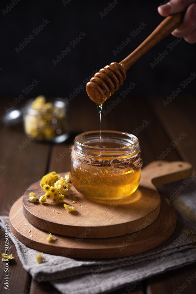 Natural floral honey drains to jar on wood background. Front view Natural floral honey drains to jar on wood background. Front view
