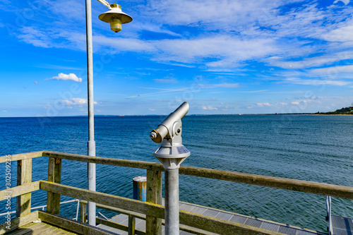 Telescope with coin slot and lantern on the pier in Bansin on the island of Usedom in Germany. Sea and sky are dark blue and radiate in the sunshine.