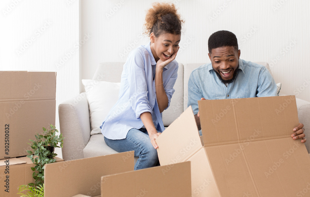 Excited Couple Unpacking Boxes Sitting On Sofa In New Apartment Excited Couple Unpacking Boxes Sitting On Sofa In New Apartment