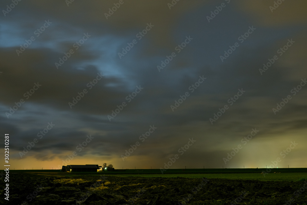 Stormcloud with falling rain streaks over a farm in the dutch countryside at dusk