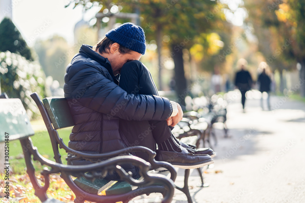 Worried young man on a bench during autumn day - obrazy, fototapety, plakaty 