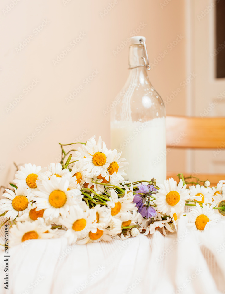Simply stylish wooden kitchen with bottle of milk and glass on table, summer flowers camomile, healthy foog moring concept close up Simply stylish wooden kitchen with bottle of milk and glass on table, summer flowers camomile, healthy foog moring concept close up