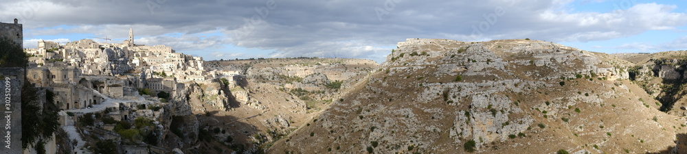 Panoramic view of the Sassi of Matera with tuff stone houses. Mountains with sky and clouds.