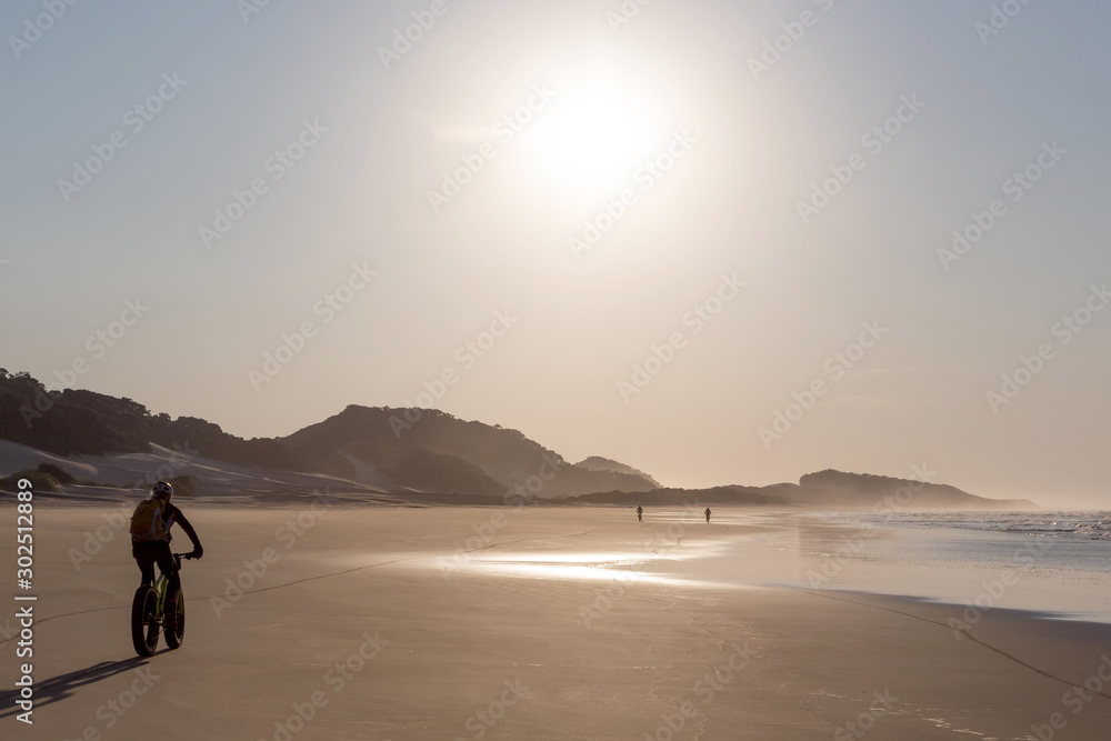 Cyclists riding into the sun along a deserted beach Cyclists riding into the sun along a deserted beach