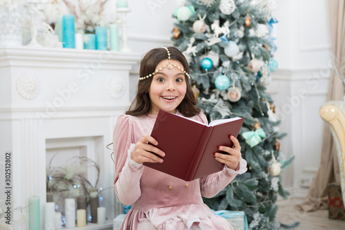 What do you fantasy for New Year. Happy girl hold fantasy book at xmas tree. Christmas child read fantasy story. Kids fantasy and imagination. Fairy tale