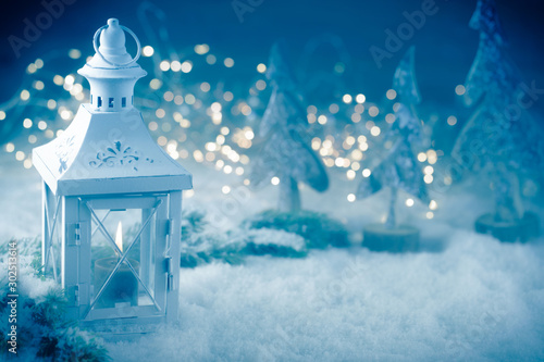 Vintage Christmas lantern with burning candle in grey blue snow landscape with magic bokeh lights - Monochrome Xmas background - Greeting card - Advent candle