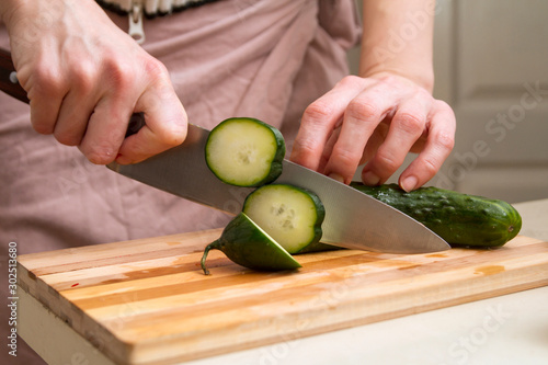 Female Chef Slices a fresh cucumber with a sharp knife on a kitchen table photo