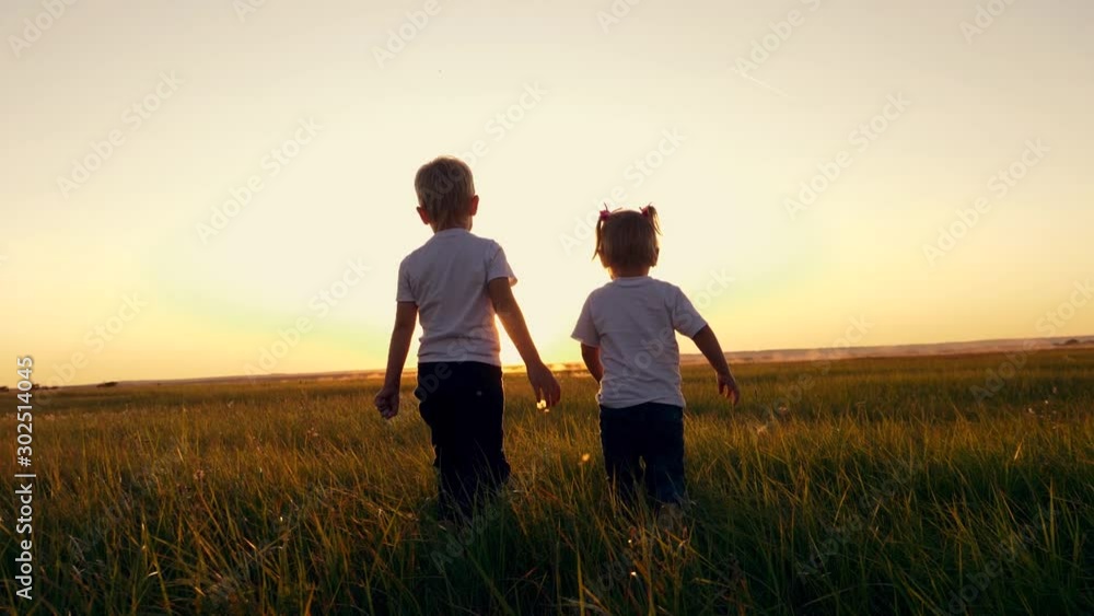 Children boy and girl walking on the green grass holding hands. Children boy and girl walking on the green grass holding hands.