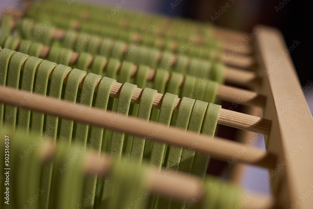 Naklejka premium Grüne Nudeln Tagliatelle mit Spinatfärbung beim Trocknen auf Holzständer