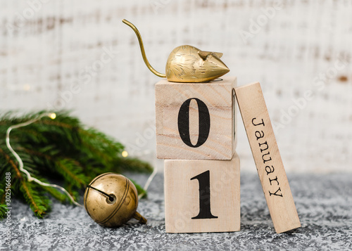 Chinese New Year 2020. Date January 1 on a wooden calendar with metal rat and christmas bell and twigs of a Christmas tree on agrey background. New Year of the rat. photo