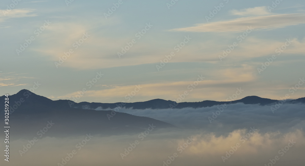 Sea of clouds at sunrise between mountains with some lenticular cloud in the sky