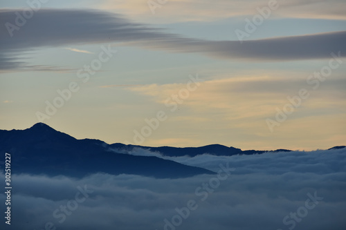 Sea of clouds at sunrise between mountains with some lenticular cloud in the sky