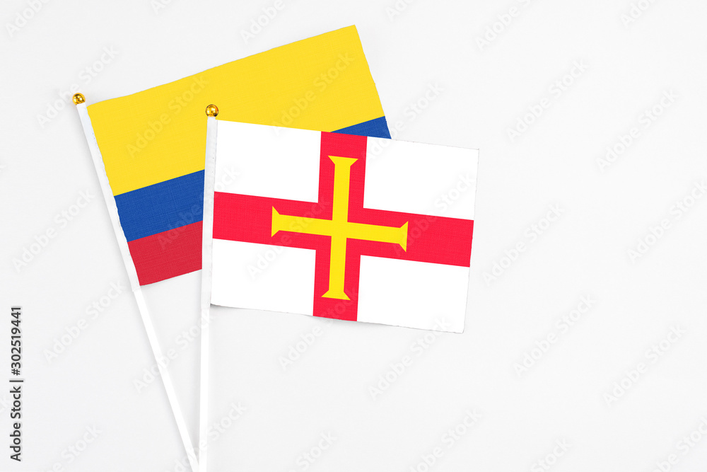 Guernsey and Colombia stick flags on white background. High quality fabric, miniature national flag. Peaceful global concept.White floor for copy space.