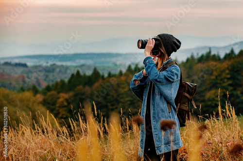 Canvas Style girl with camera and backpack at countryside with mountains on background
