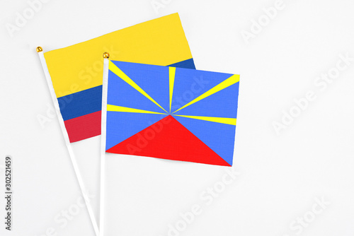 Reunion and Colombia stick flags on white background. High quality fabric, miniature national flag. Peaceful global concept.White floor for copy space.