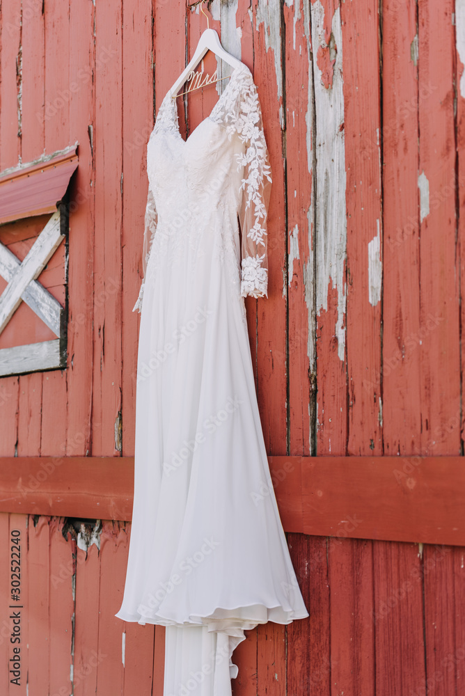 White wedding dress hanging in front of red barn