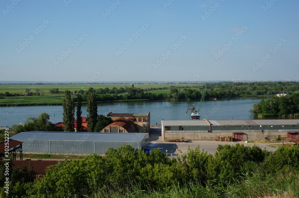 Warehouse facilities on the port territory. Port crane on the river Bank. Summer natural landscape.