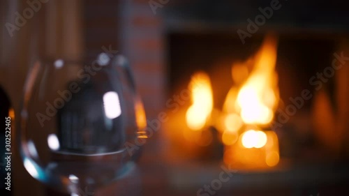Focus and camera move from the fireplace with flaming fire to a bottle of red wine and a wine glass. Alcoholic drink concept. Fire background. Drink alone. Restaurant Beverage. Beverage Close up