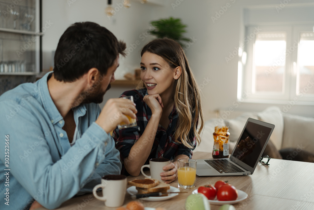 Young smiling couple communicating during breakfast time in the kitchen