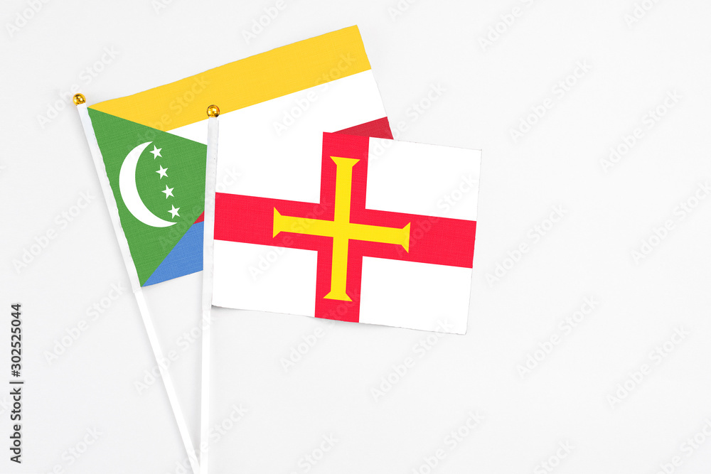 Guernsey and Comoros stick flags on white background. High quality fabric, miniature national flag. Peaceful global concept.White floor for copy space.