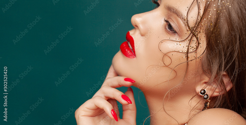 Close-up portrait of beautiful woman with holiday make-up. Perfect red lips and nail design. Gold glitters on her face. Christmas make-up - obrazy, fototapety, plakaty 