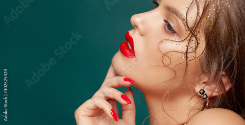 Close-up portrait of beautiful woman with holiday make-up. Perfect red lips and nail design. Gold glitters on her face. Christmas make-up