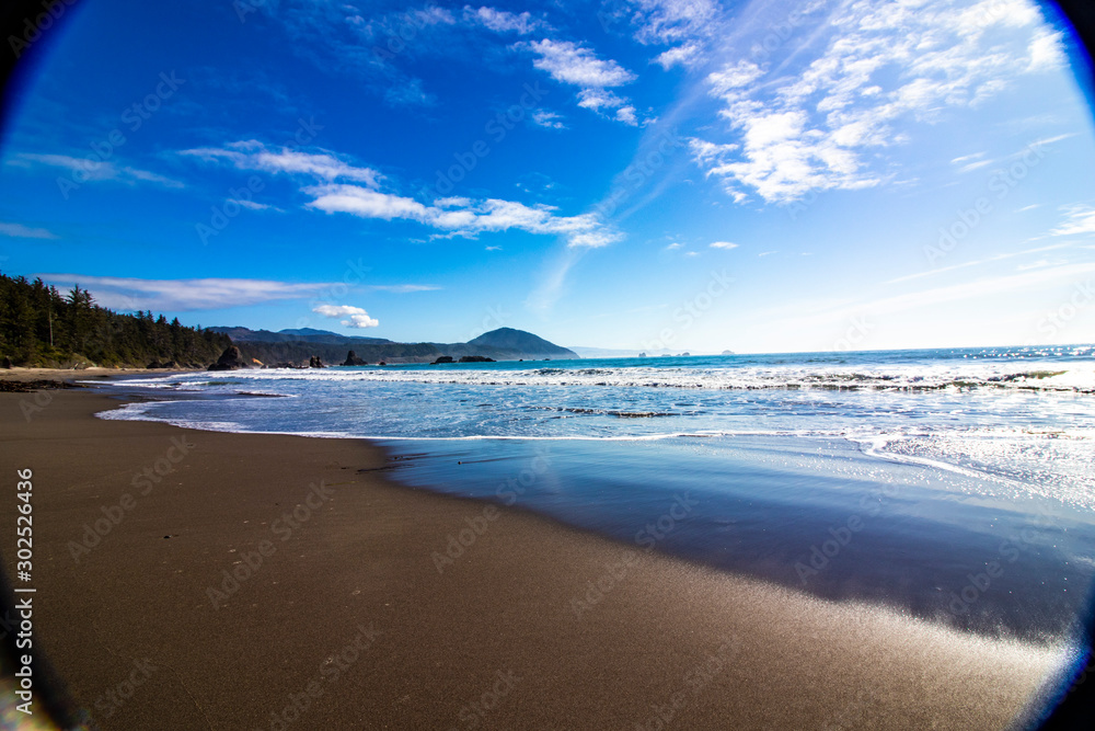 Pacific ocean photography effect, clear water, huge sandy beach, dramatic blue sky and mountains in background on US route 1 California, sunlight and sunbeam effect