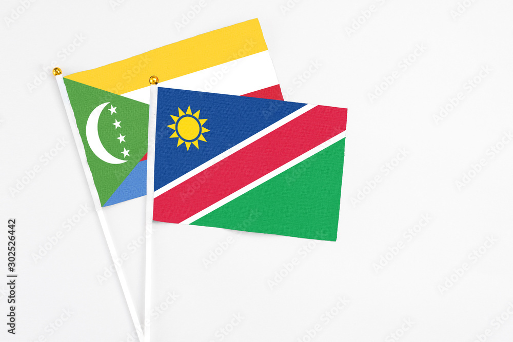 Naklejka premium Namibia and Comoros stick flags on white background. High quality fabric, miniature national flag. Peaceful global concept.White floor for copy space.
