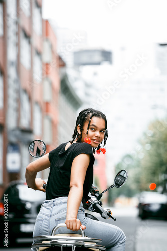 Cheerful young african-canadian woman driving a scooter on the city street of Montreal.