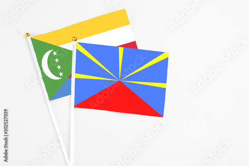 Reunion and Comoros stick flags on white background. High quality fabric, miniature national flag. Peaceful global concept.White floor for copy space.