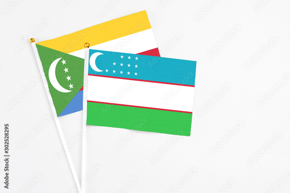 Uzbekistan and Comoros stick flags on white background. High quality fabric, miniature national flag. Peaceful global concept.White floor for copy space. Uzbekistan and Comoros stick flags on white background. High quality fabric, miniature national flag. Peaceful global concept.White floor for copy space.