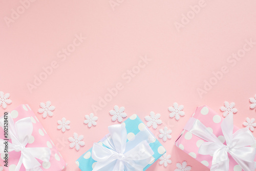 Holiday background , pink and blue gift boxes in polka dots with white ribbon and bow on a pink background with snowflakes , flat lay, top view