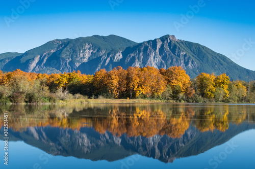 The calm, still waters of a large pond near Snoqualmie, Washington reflect the beautiful fall colors of shoreline trees and Mt. Si in the distant background.