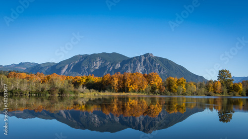 The calm, still waters of a large pond near Snoqualmie, Washington, reflect the beautiful fall colors of shoreline trees and Mt. Si in the distant background. 16 x 9 crop.