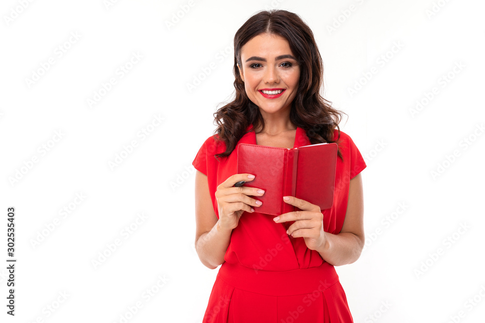 A young woman with bright makeup, in a red summer dress stands with a notebook and smiles A young woman with bright makeup, in a red summer dress stands with a notebook and smiles