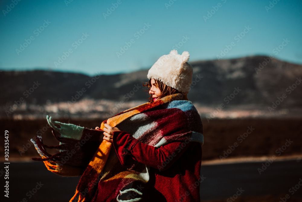 Obraz premium .Pretty young woman enjoying a sunny winter day outdoors. Surrounded by nature, relaxed and carefree. Covering from the cold with a burgundy scarf and wearing a fur hat. Lifestyle