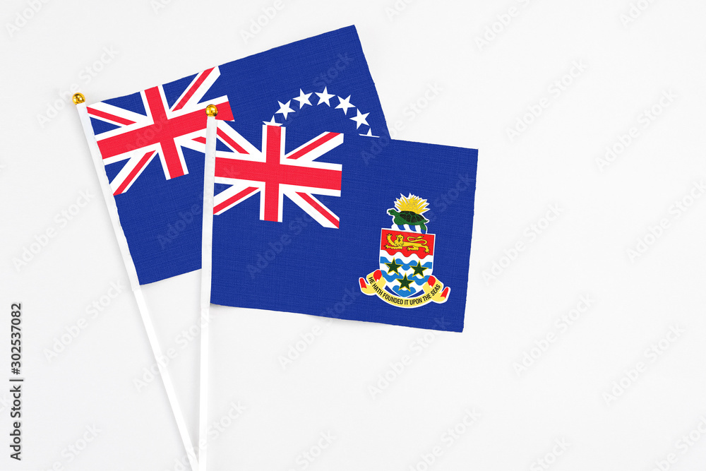 Fototapeta premium Cayman Islands and Cook Islands stick flags on white background. High quality fabric, miniature national flag. Peaceful global concept.White floor for copy space.