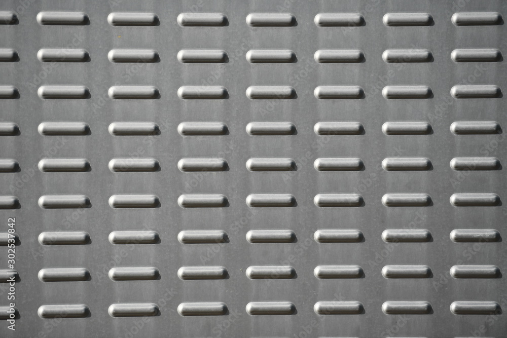 A gray plate with many short lines in a row. A structured metal wall. A gray plate with many short lines in a row. A structured metal wall.