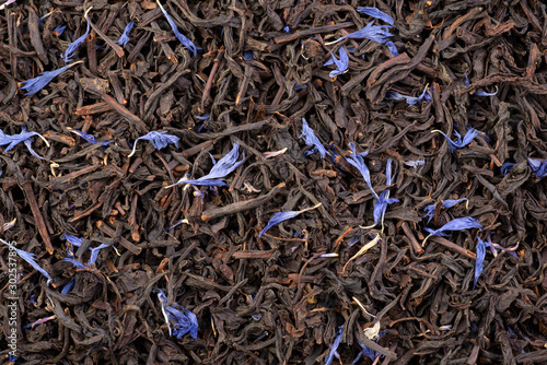 Earl grey with corn flower petals, black dry tea leaves background