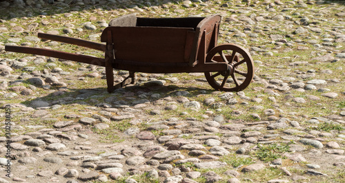 An old wooden wheelbarrow with one wheel stands on the paving stones.