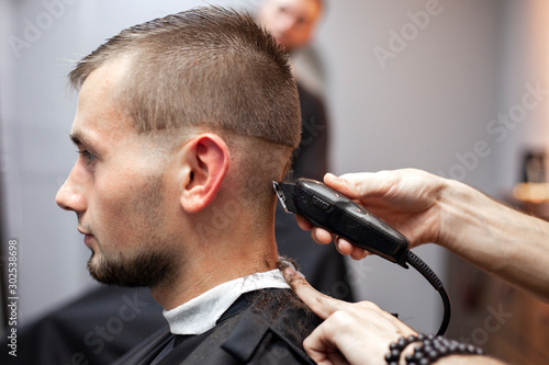 young guy makes a short haircut in a barbershop with a trimmer, close-up